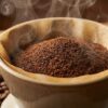 挽きたてのコーヒー粉がドリッパーに山盛りになり、そこから豊かな湯気とアロマが立ち上っているクローズアップ写真。周囲には焙煎されたコーヒー豆が散らばっている。
