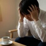 コーヒーを飲み過ぎて大量が悪くなり、頭を抱えている男性