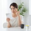 鏡を見て肌の不調に気づき、不安そうな表情を浮かべる日本人女性。隣にはマグカップに入ったコーヒーと水がある。