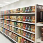 家電量販店の明るい棚に陳列された、様々な種類のキューリグ K-Cup コーヒーカプセルの箱。