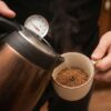 温度計付きのケトルを使って、マグカップ内のインスタントコーヒーにお湯を注ぐ様子。適切な温度管理でおいしい入れ方を実践しているシーン。